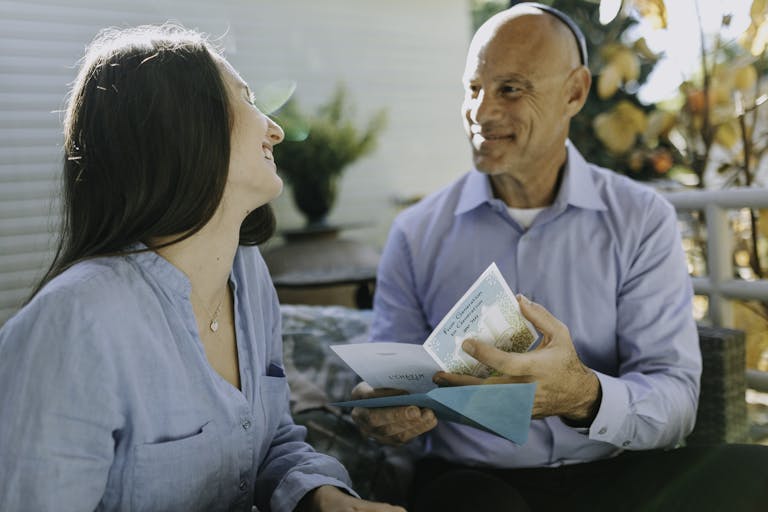 Father and daughter enjoy Hanukkah by exchanging gifts and smiling indoors.